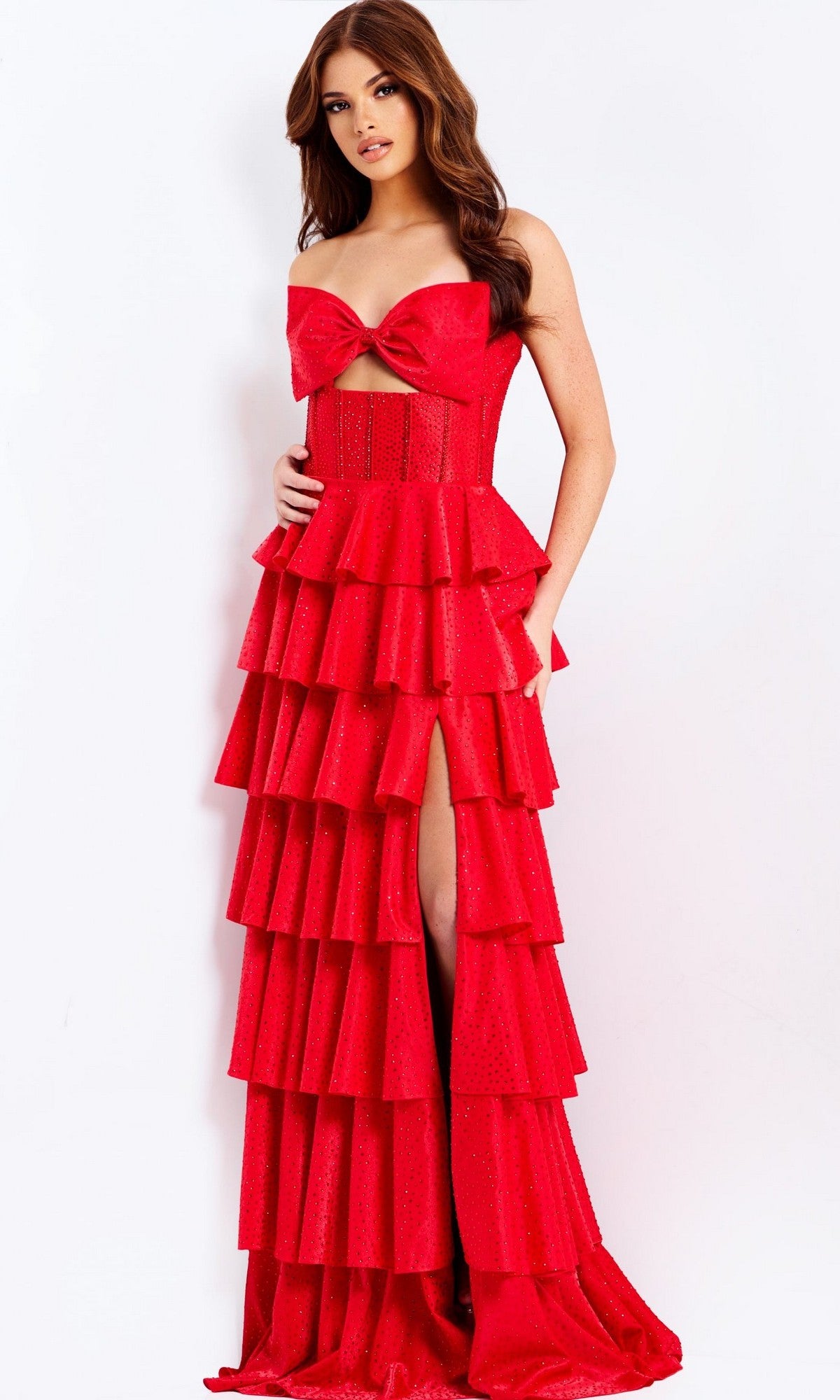 A woman models the Jovani 49780 long red prom dress with a strapless sweetheart neckline, large bow bodice, tiered ruffles, and high slit, standing against a plain white background.